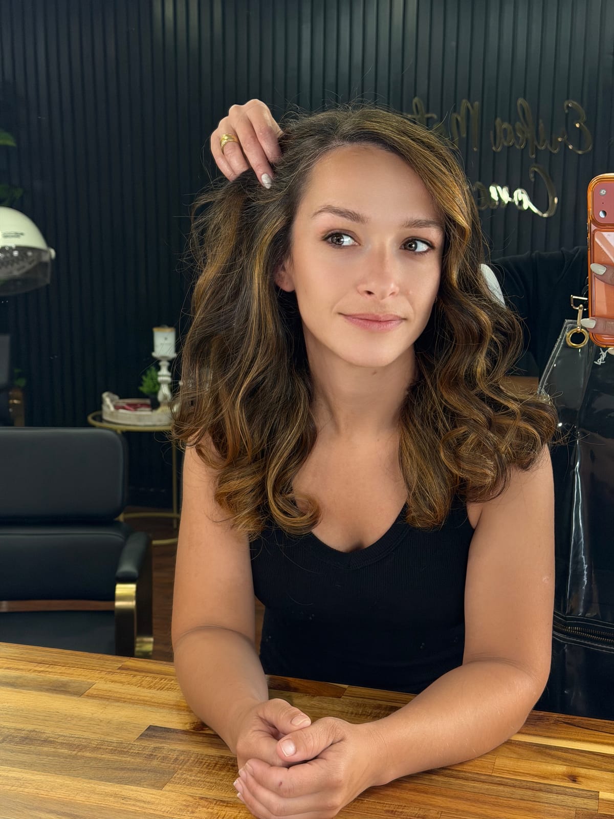 Cliente sorrindo com castanho iluminado e ondas, na bancada do salão